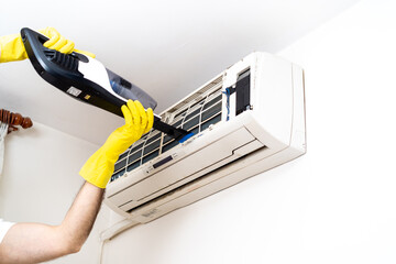 Hand in yellow glove and vacuum cleaner pipe. Technician service using vacuum cleaner to cleaning the air conditioner