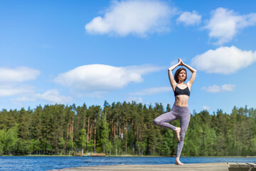 Woman practicing yoga on a lake standing on log in yoga tree pose. fitness lifestyle at the outdoors nature background. Sunny day. copy space 