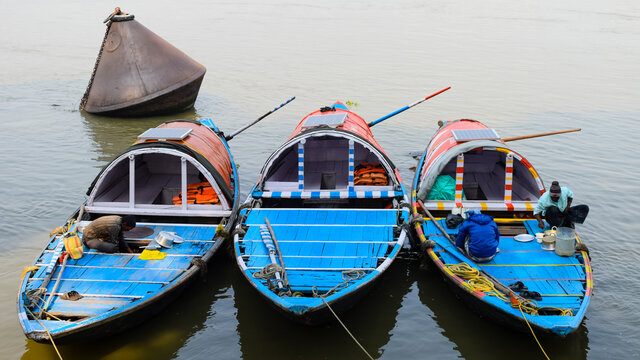 INDIA, KOLKATA, 9th FEBRUARY 2020: Three boats are anchored on bank of river ganga have a solar panel for lighting and unrecognisable fishermen preparing breakfast on it.