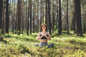 Woman practicing yoga in forest with namaste behind the back. fitness lifestyle at the outdoors nature background. Sunny day in pine forest. copy space