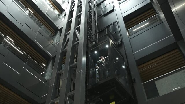 A view of young confident successful businesswoman riding down in transparent elevator and talking at phone.