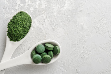 Fototapeta na wymiar Chlorella or spirulina in the form of tablets and powder on a gray concrete background.