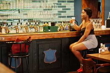 Portrait of african american woman, retro hairstyle posing at restaurant on bar counter with cup of latte.