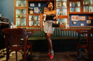 Portrait of african american woman, retro hairstyle posing at restaurant with cup of latte.