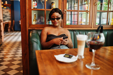 Portrait of african american woman, retro hairstyle posing at restaurant with cup of latte.
