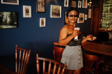 Portrait of african american woman, retro hairstyle posing at restaurant with cup of latte.