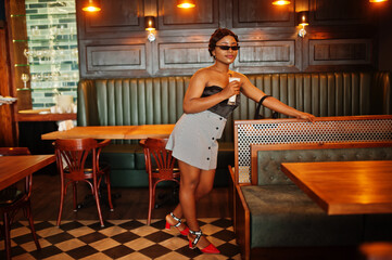 Portrait of african american woman, retro hairstyle posing at restaurant with cup of latte.