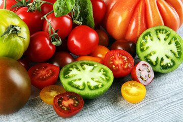 various colorful tomatoes and basil leaves on rustic table.