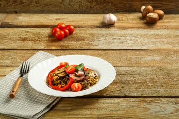 On a wooden table is a dish of mung bean with vegetables and mushrooms on a napkin and a fork. Copy space.