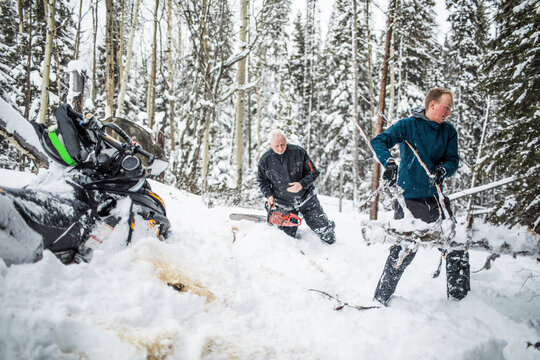 Father and son clearing trails while snowmobiling.