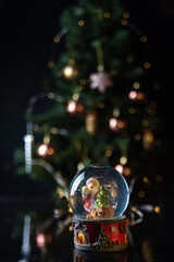 Christmas scene with tree, lights and snow globe. Selective focus on black background.