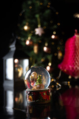 Christmas scene with tree, lights and snow globe. Selective focus on black background.