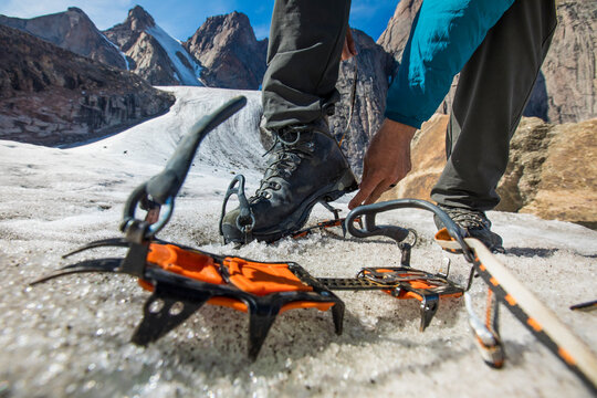 Climber straps on crampons to his mounatineering boots on glacier.