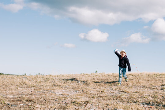 young boy running with a kite at the top of a hill on a sunny day