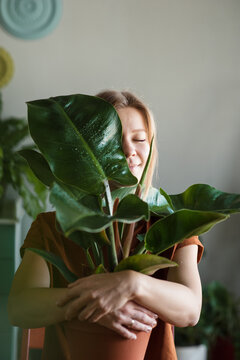 Woman hugs potted plant with big leaf wich closes her half of face