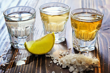 Mexican gold and silver tequila and lime salt on wood background