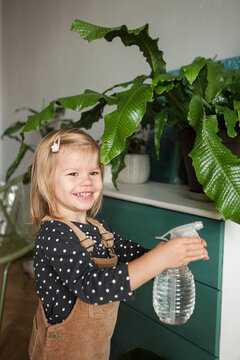 Smiling child with water sprayer in hands watering plants at home