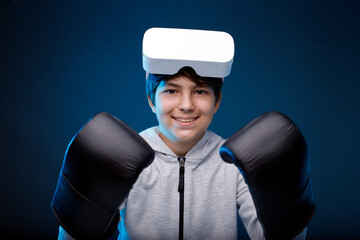 Portrait of young boy in glasses of virtual reality, boxing gloves and hoodie on dark background. Augmented reality, future technology concept. VR. Blue neon light.