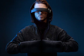 Model young man with beard in glasses of virtual reality, boxing gloves and hoodie on dark background. Augmented reality, future technology concept. VR. Blue neon light.