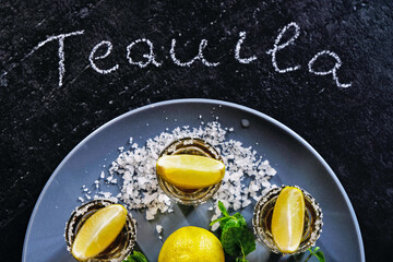 Gold tequila shot with lime and sea salt on grey plate.