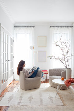 Woman reading in modern chair in bright, white living space