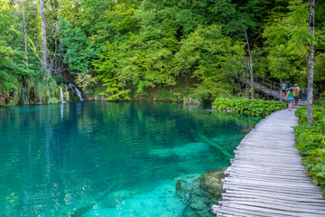 Fototapeta na wymiar Beautiful crystal clear lake with wooden walking path at Plitvice Lakes National Park in Croatia. Clean turqoise water cascade in the Balkans. Lake with small fish swimming inside. Tourist attraction