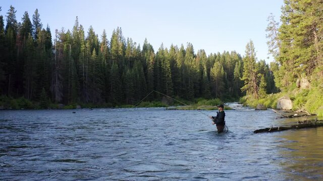 Active male adult in waist deep river water fly fishing with pole in Oregon