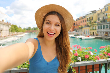 Pretty young tourist woman takes self portrait on Lake Garda, Italy. Beautiful fashion girl takes selfie photo in Peschiera del Garda, Italy.