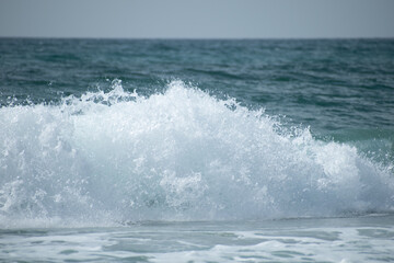Small cresting wave in the Atlantic Ocean on the coast. Blue green ocean waves with sea foam and salt water spray. Beach travel photos.