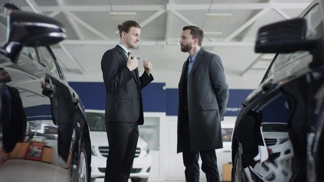 Handsome man is talking to the car dealer choosing auto. Auto dealer is working with his customer at the dealership showing a new automobile.