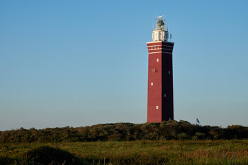 Ouddorp lighthouse, red tower with white top, blue sky and green meadow. Netherlands