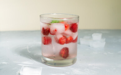 Homemade frozen strawberry lemonade with ice cubes and a sprig of mint on a gray background. A refreshing summer drink. Copy space.