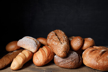 Variety of loaves of bread and buns on wooden table background