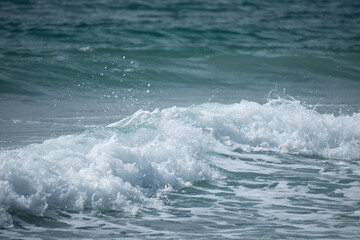 Small cresting wave in the Atlantic Ocean on the coast. Blue green ocean waves with sea foam and salt water spray. Beach travel photos.