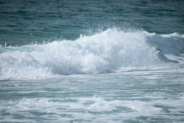 Small cresting wave in the Atlantic Ocean on the coast. Blue green ocean waves with sea foam and salt water spray. Beach travel photos.