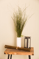 Natural wooden table in a modern style in beige tones with a vase of dried flowers and a copper lamp.