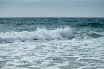 Small cresting wave in the Atlantic Ocean on the coast. Blue green ocean waves with sea foam and salt water spray. Beach travel photos.
