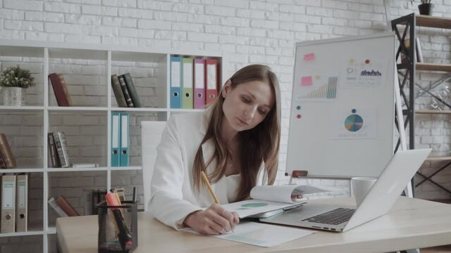 business woman looks statistics while sitting at office desk. in a bright office there is a flipchart with piechart and statistics