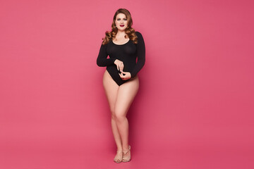 Young plump woman with makeup and trendy hairstyle wearing a black bodysuit and posing at the pink...