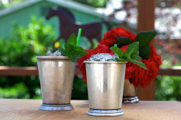 Mint julep drinks in silver cups with red roses and horse silhouette in background - obrazy, fototapety, plakaty