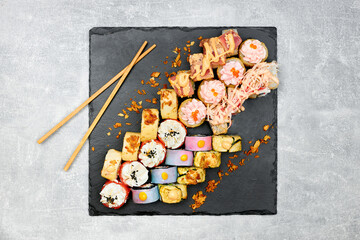Fresh fish sushi set with side dishes on a black graphite board and gray background