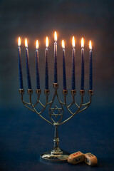 Burning blue candles on a Jewish menorah at Hanukkah with a dreidel on a dark blue background