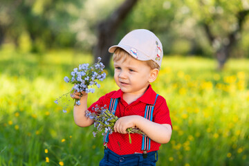 child boy has fun playing in nature among flowers and collects a bouquet