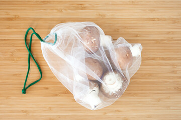 Fresh organic vegetables mushrooms in zero waste shopping bag on wooden table background flat lay