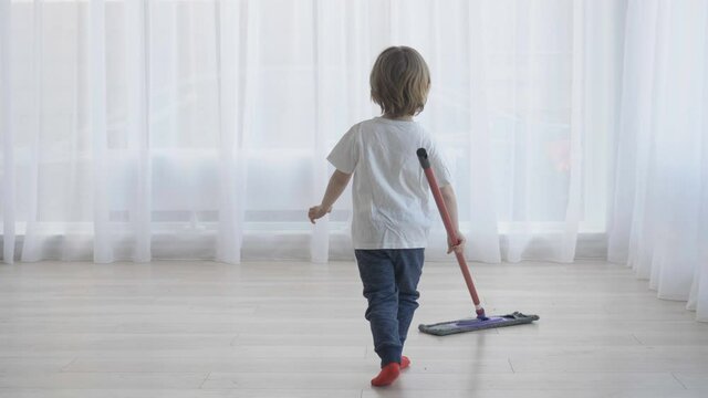 Little blond hair child running with mop on floor, funny enthusiastic house worker