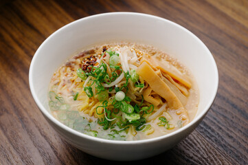 tonkotsu pork broth ramen noodle soup with bamboo shoots, bean sprouts, scallion in a white bowl on wooden table