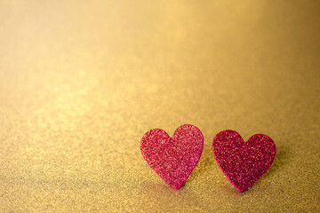 Two red hearts like a couple on a gold glitter and sequin background that sparkles and has lots of copy space
