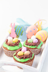 Homemade carrot cake muffins decorated with cream cheese frosting and easter chocolate eggs, on wooden tray, vertical