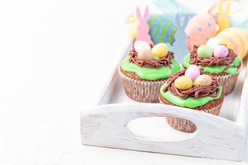 Homemade carrot cake muffins decorated with cream cheese frosting and Easter chocolate eggs, on wooden tray, horizontal, copy space