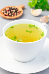 Chicken broth in  white cup garnished with chopped parsley, vertical, closeup